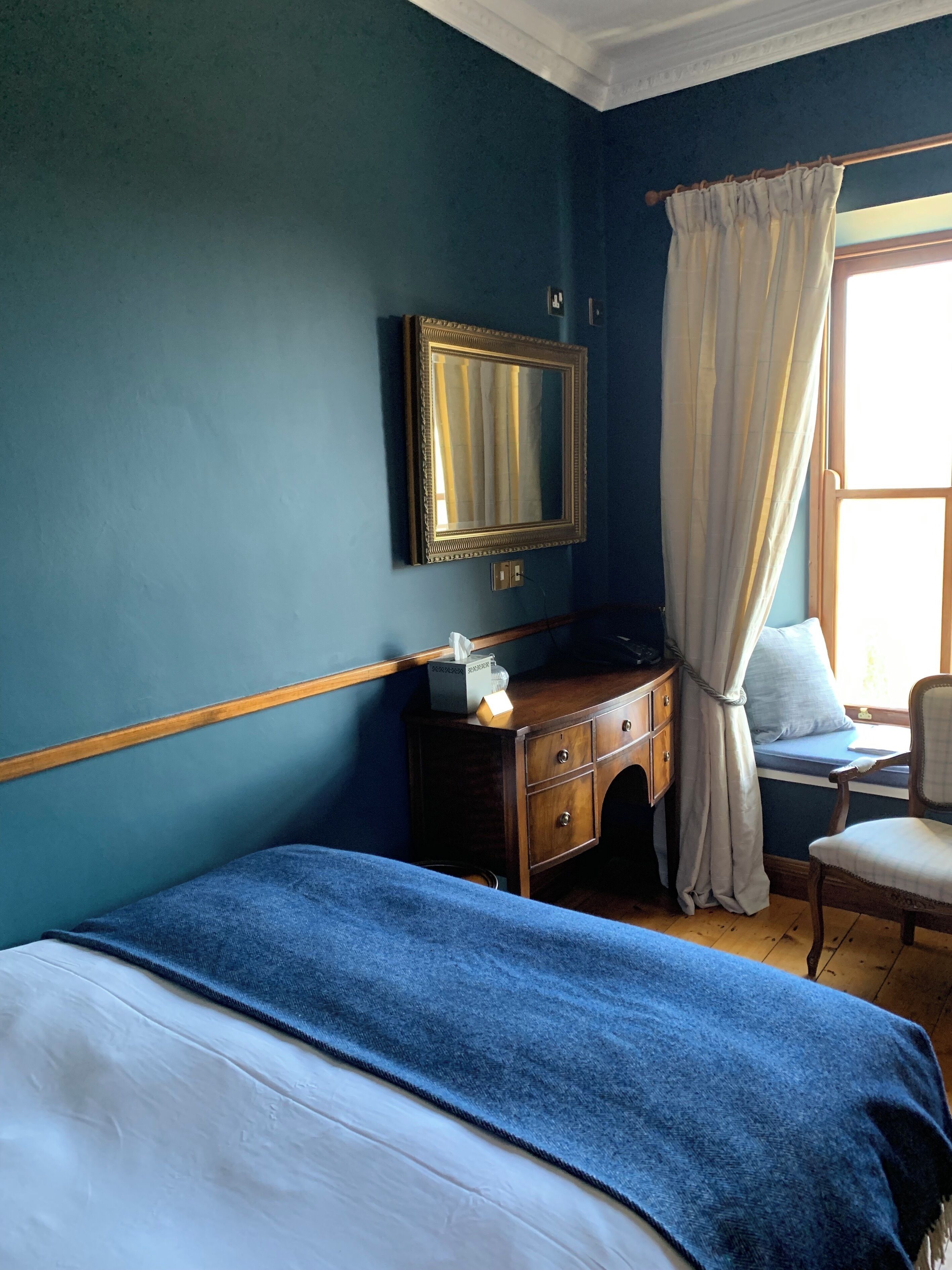 Un dormitorio con cama, cómoda, silla, ventana con cortinas y un espejo en la pared.