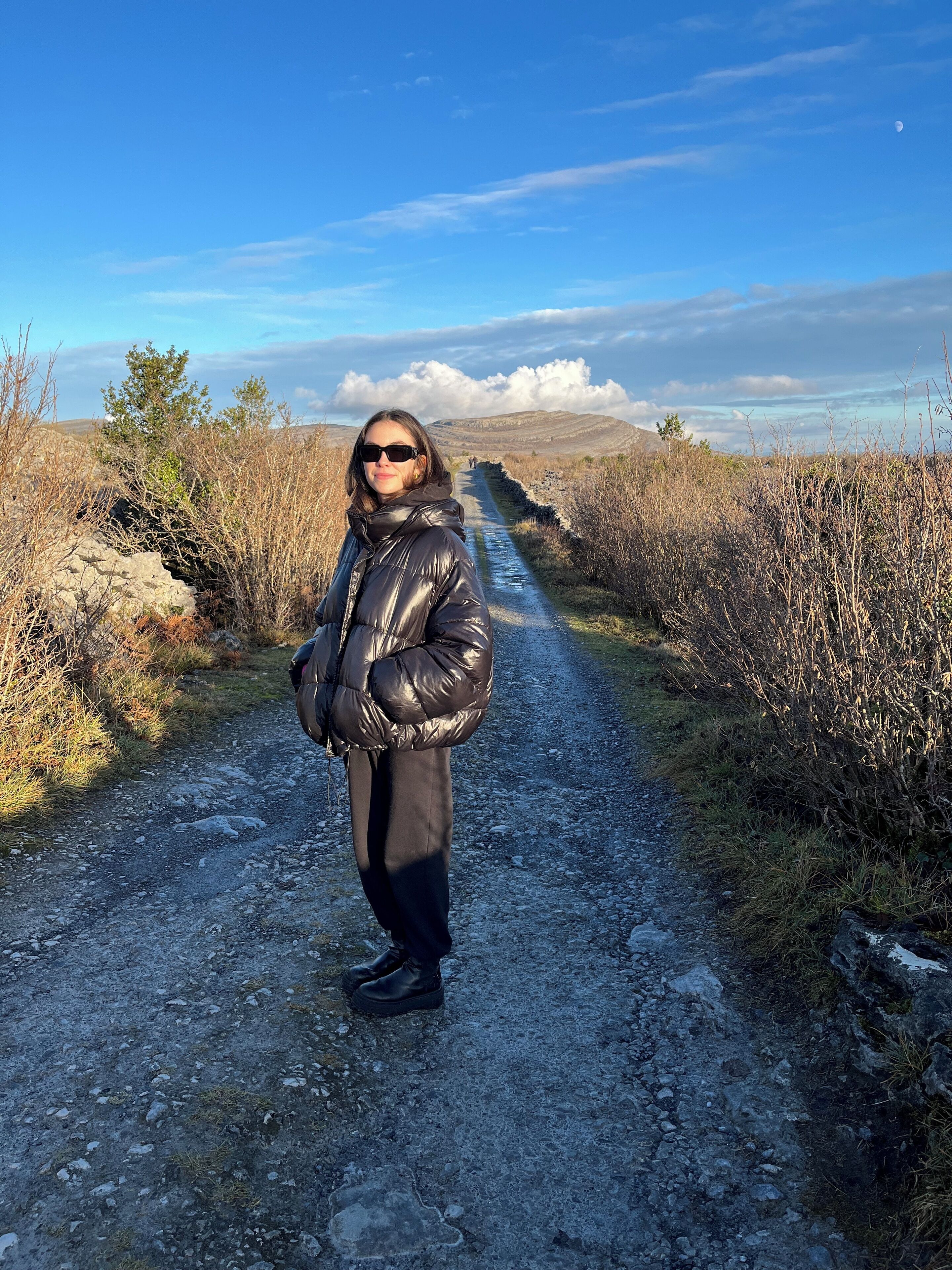 A person standing on a gravel road with a clear sky and distant hills.