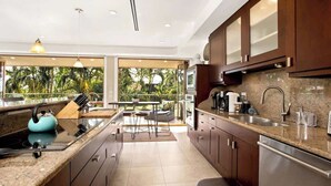 A modern kitchen with dark wooden cabinets, stainless steel appliances, and a large island with a kettle. - Aloha Villas # 4, Luxury Oceanfront Townhouse, Ste (Kihei)