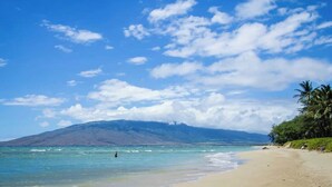 A beach with clear skies, calm waters, and a mountain in the background. - Aloha Villas # 4, Luxury Oceanfront Townhouse, Ste (Kihei)