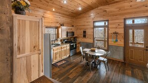 Interno di una baita in legno con cucina, zona pranzo e un'ampia porta di legno.