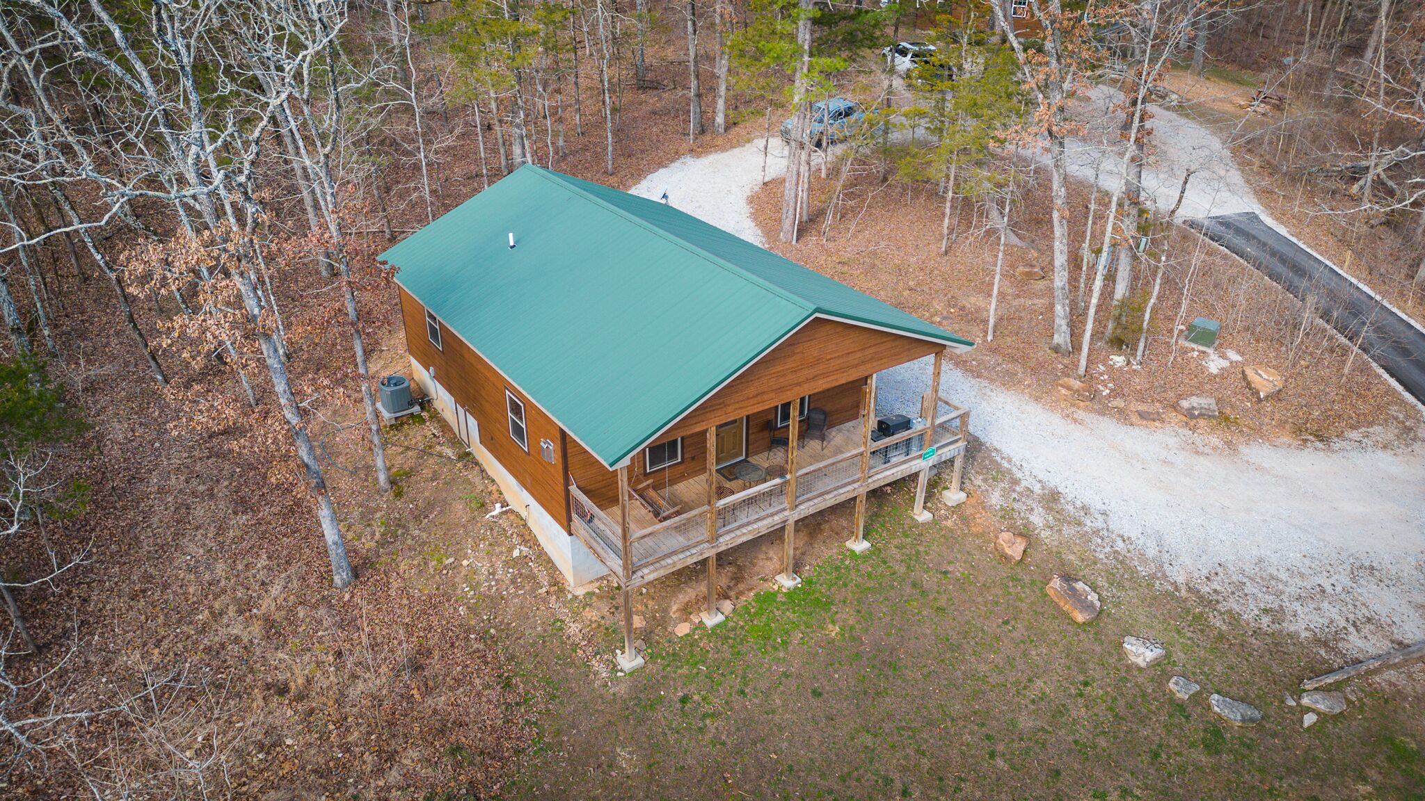 A wooden cabin with a green roof, a porch, and a gravel driveway.