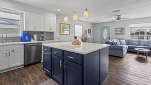 A modern kitchen with white cabinets, a blue island, and pendant lighting.