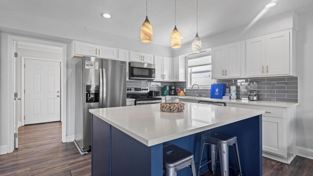 A modern kitchen with white cabinets, stainless steel appliances, a large island with stools, and pendant lighting.