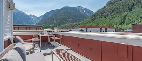 Terraza en la azotea con mobiliario exterior, una mesa y vistas a las montañas.