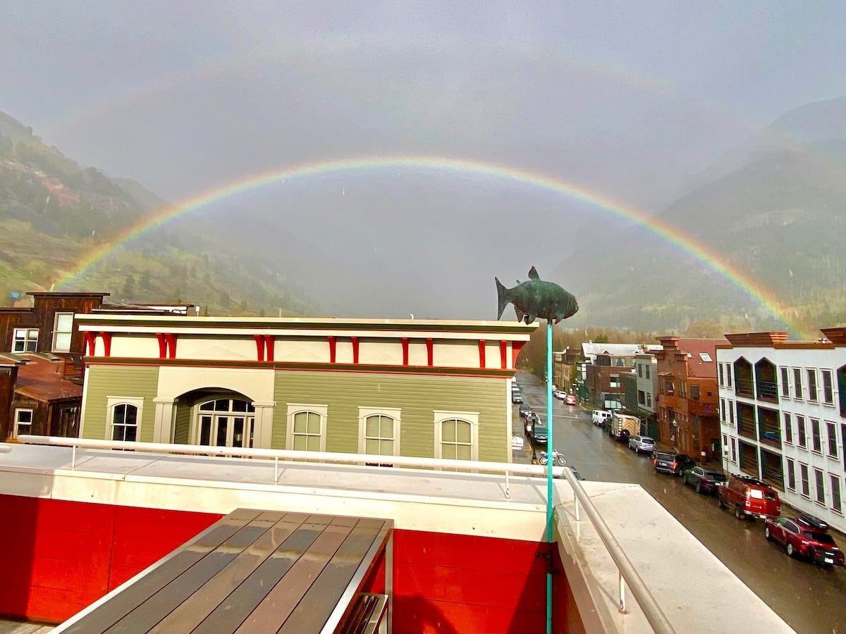 A building with a green facade and red trim, a parking lot, and a rainbow in the background.