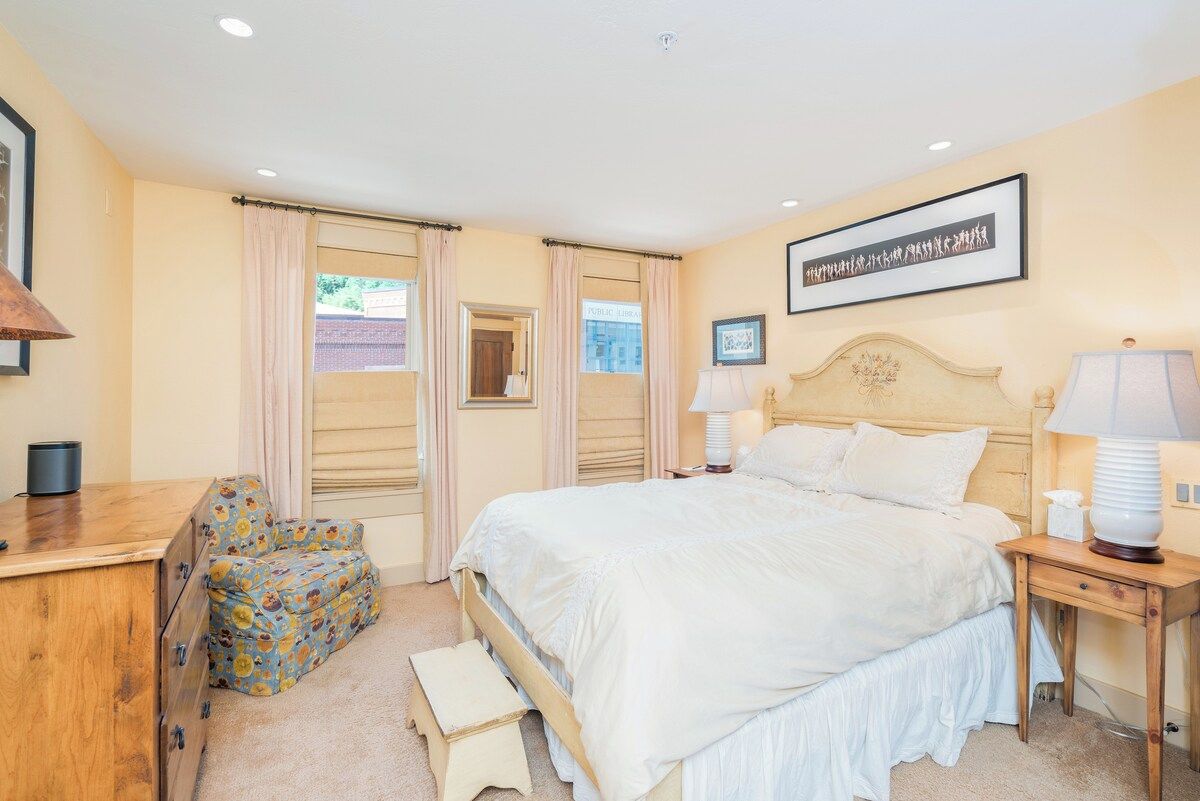 A bedroom with a bed, bedside tables, a chair, a dresser, and a window with curtains.