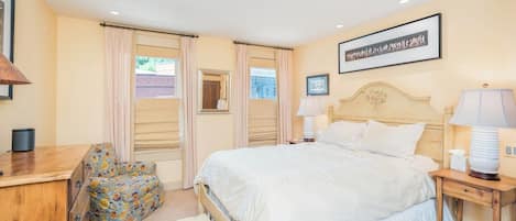 Une chambre à coucher avec un lit, des tables de chevet, une chaise, une commode et une fenêtre avec des rideaux.