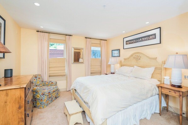 A bedroom with a bed, bedside tables, a chair, a dresser, and a window with curtains.