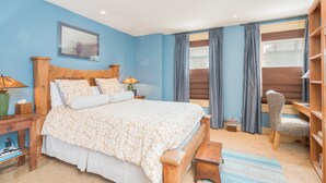 Une chambre à coucher avec un grand lit, une tête de lit en bois, une table de chevet avec une lampe, une chaise, un bureau et une bibliothèque.