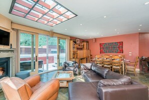 A spacious living room with a fireplace, leather sofas, a glass coffee table, and a dining area with wooden chairs and a table.