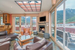A spacious living area with leather sofas, a glass coffee table, a fireplace, and a large window offering a mountain view.