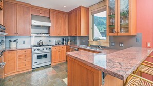 Une cuisine dotée de meubles en bois, d’un comptoir en granit, d’une hotte de cuisinière en acier inoxydable et d’une grande fenêtre offrant une vue sur l’extérieur.