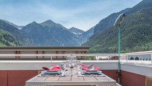 Une table à manger dressée avec des assiettes, des verres et une bouteille, donnant sur un paysage montagneux.