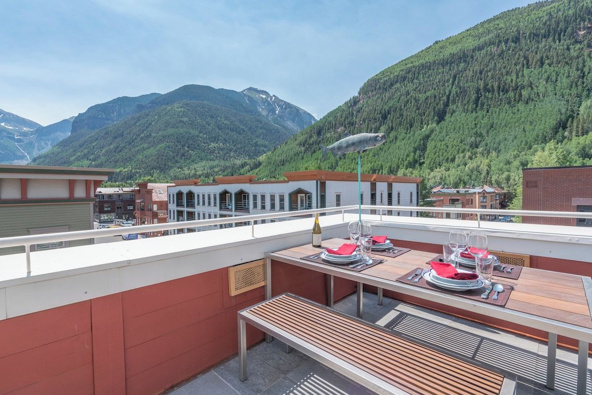 Eine Terrasse mit Esstisch, mit Blick auf eine gebirgige Landschaft.