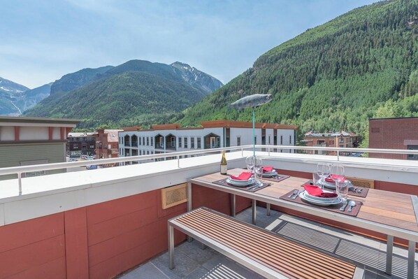 A terrace with a table set for dining, overlooking a mountainous landscape.