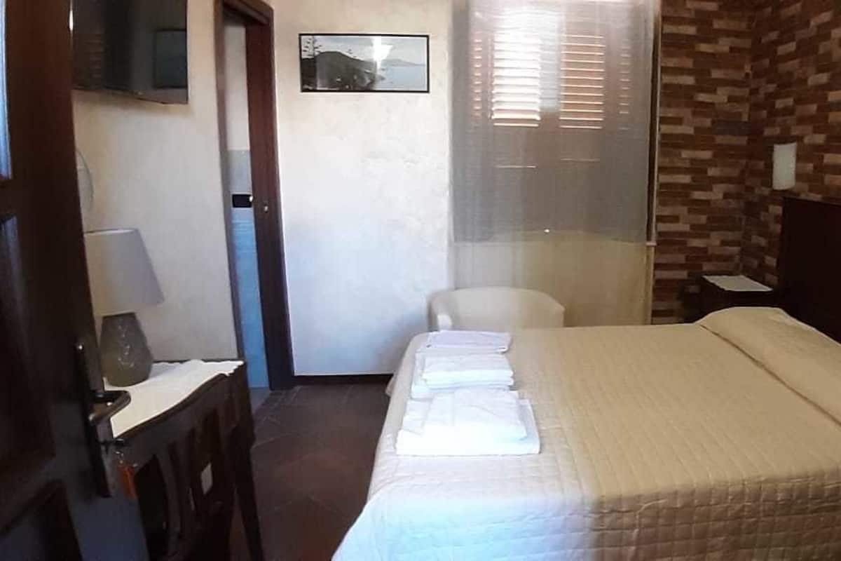 A hotel room with a bed, a chair, a desk with a lamp, and a window with blinds.