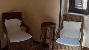 A room with two wicker chairs, a small stool, patterned floor tiles, and two framed pictures on the wall. - B&B Rivellini (Tropea)
