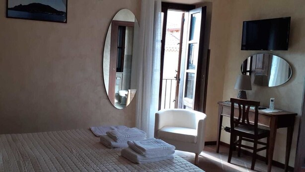 A hotel room with a bed, a chair, a desk with a lamp, a TV, and a large mirror. - B&B Rivellini (Tropea)