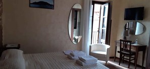 Habitación de hotel con cama, una silla, un escritorio con lámpara, televisor y un espejo grande.