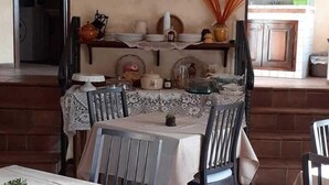 A dining area with a table set for four, a television mounted on the wall, and a kitchen visible through an archway. - B&B Rivellini (Tropea)