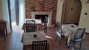 A dining area with a brick fireplace, tiled floor, and two tables with chairs. - B&B Rivellini (Tropea)
