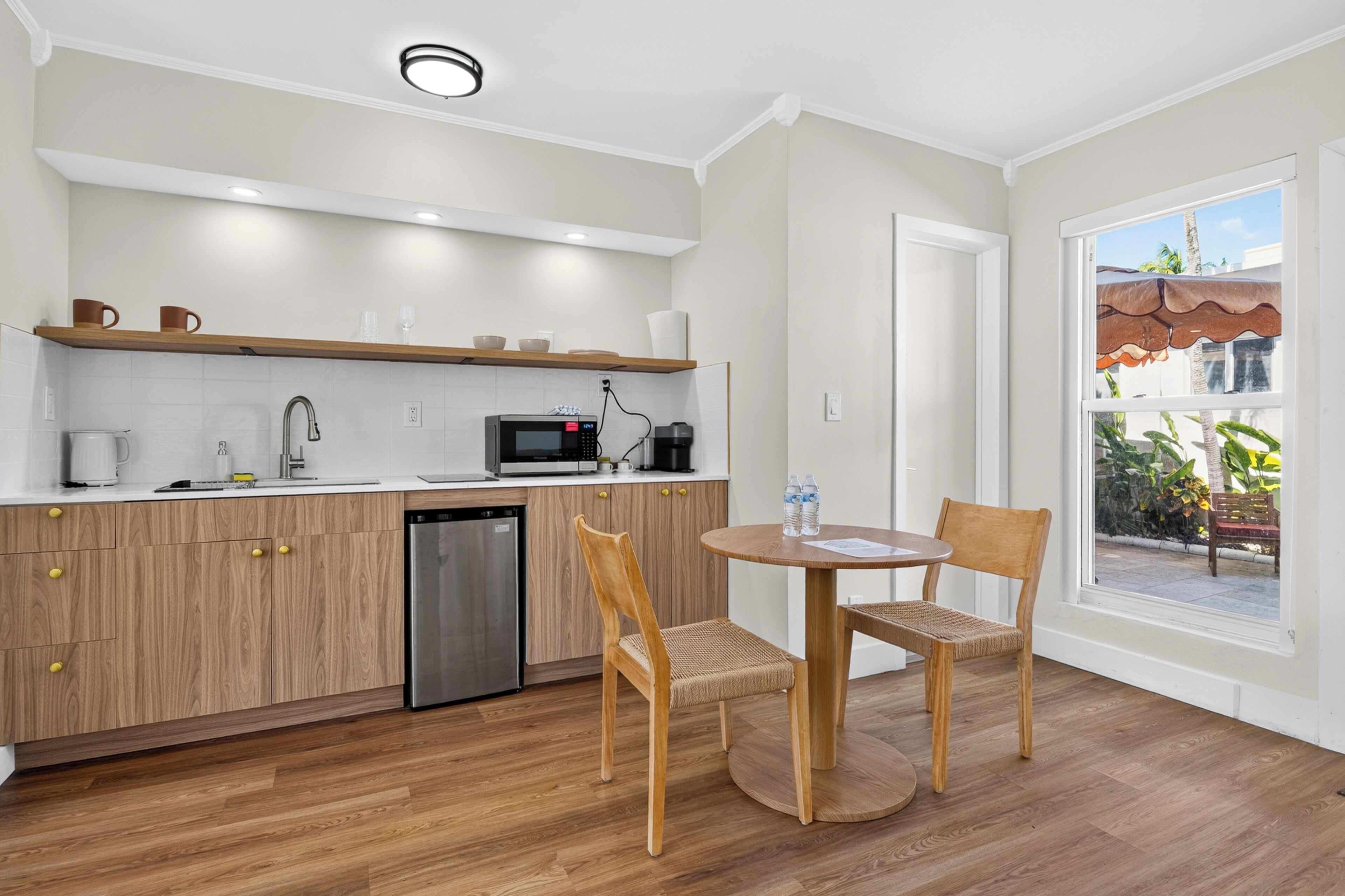 Une cuisine moderne avec des meubles en bois, un lave-vaisselle et un four à micro-ondes. On y trouve un coin repas avec deux chaises et une table, ainsi qu’une fenêtre donnant sur l’extérieur.
