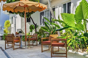 An outdoor seating area with wooden chairs and a table, surrounded by lush tropical plants. - Tiana Beach Hotel (Hollywood)