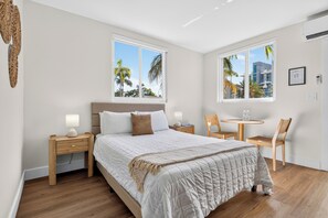 A hotel room with a bed, two bedside tables, a chair, a small table, and two windows with a view of palm trees. - Tiana Beach Hotel (Hollywood)