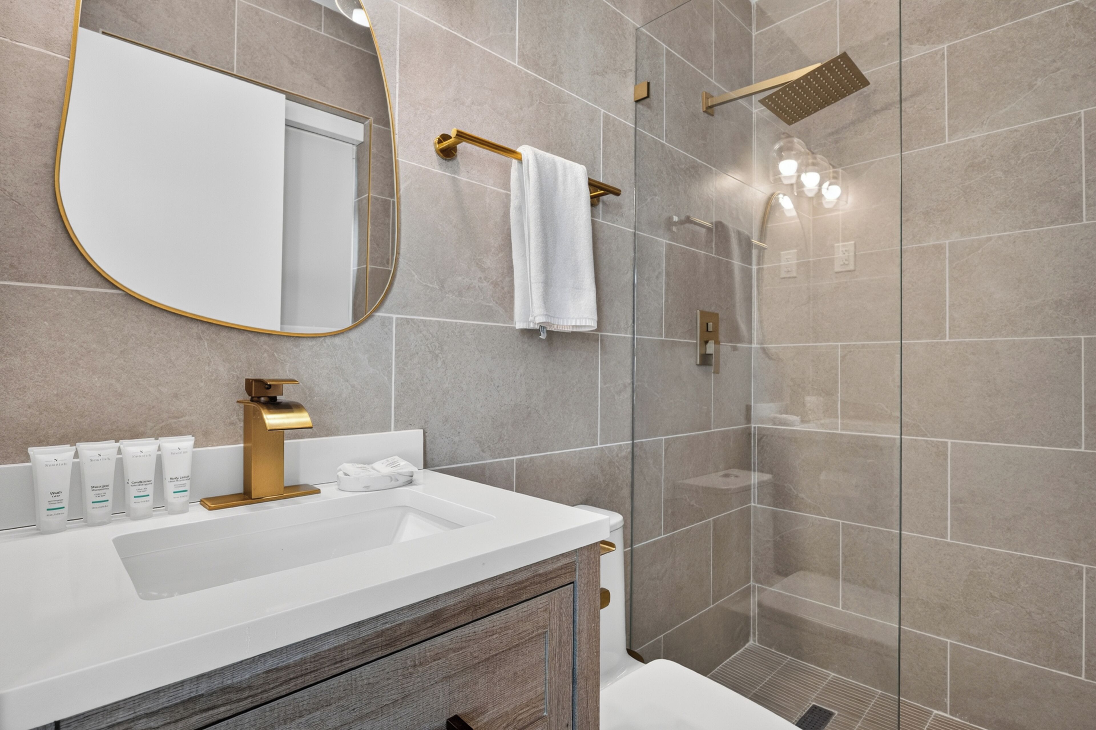 Un baño moderno con lavamanos blanco, detalles dorados y cabina de ducha de vidrio.