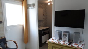 A room with a television mounted on the wall, a small table with speakers, a chair, and a door leading to a bathroom. - Rest Sea Sun comfort at 600m beach (la plaine sur mer Tharon plage)