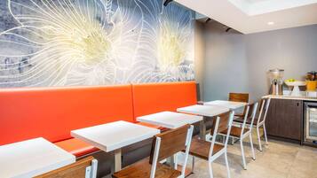 A modern restaurant with orange booths, white tables, and a large abstract mural on the wall.