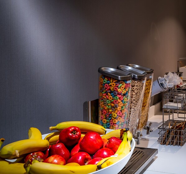 Dispensador de fruta y cereales, con plátanos y manzanas en un bol.
