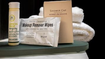 A bottle of Lemon Sage Body Lotion, a pack of Gentle Cleansing Makeup Remover Wipes, and a Shower Cap on a shelf.