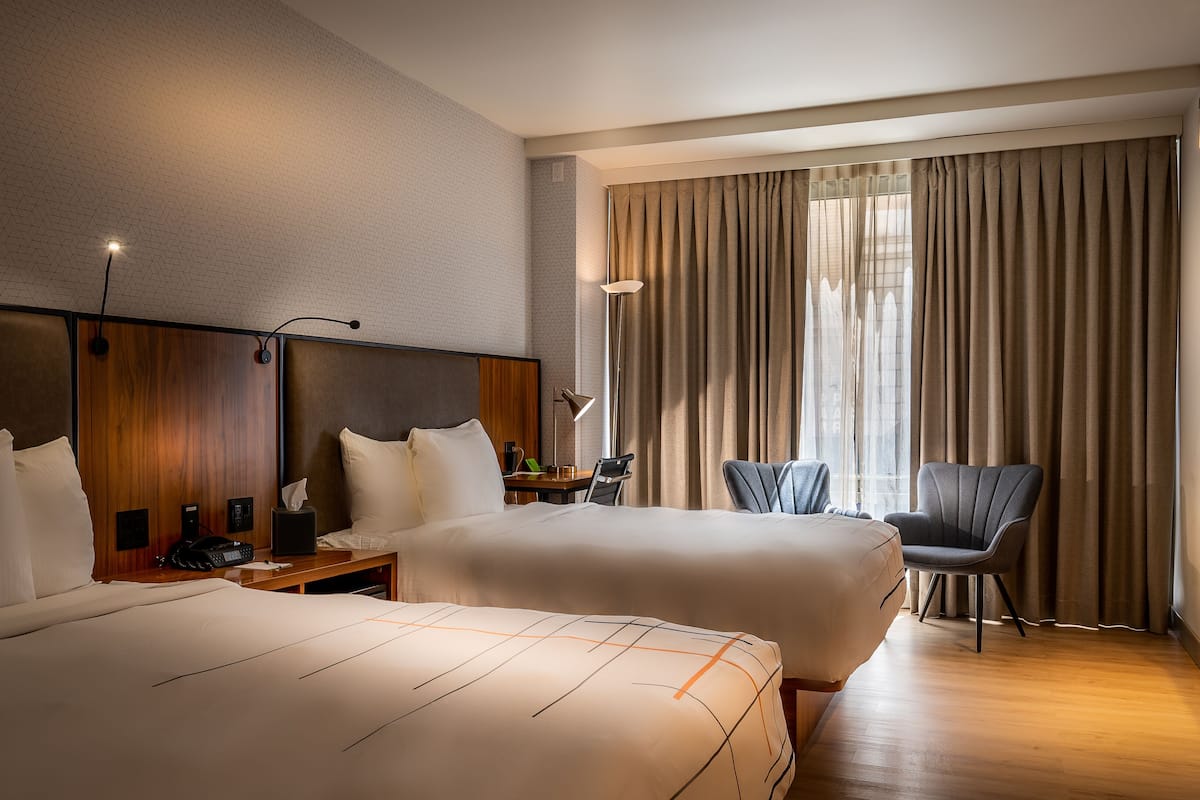 Camera d'albergo con due letti, una scrivania, una sedia, un televisore e un'ampia finestra con tende.