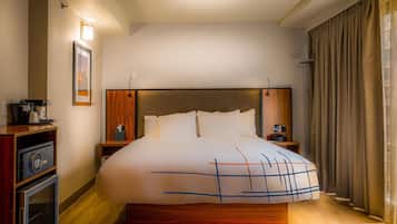 Habitación de hotel con una cama grande, una mesita de noche, una lámpara, un cuadro en la pared y una ventana con cortinas.