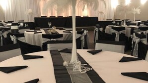 Uma sala de banquetes com mesas redondas, toalhas de mesa preta e branca e centros de mesa com plumas.