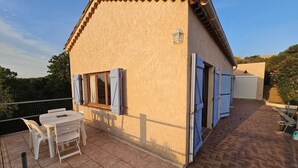 A building with a tiled patio, a table with chairs, and a small window with shutters.