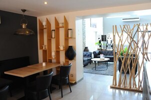 Una sala de estar moderna con comedor, que incluye una mesa de madera, sillas negras, un sofá negro y una estructura decorativa de madera.