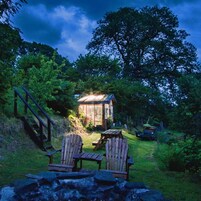 Una cabaña con terraza de madera, dos sillas Adirondack y una escalera que lleva hacia ella.