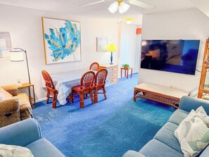 A living room with a blue carpet, a television, a dining table with chairs, and a sofa.