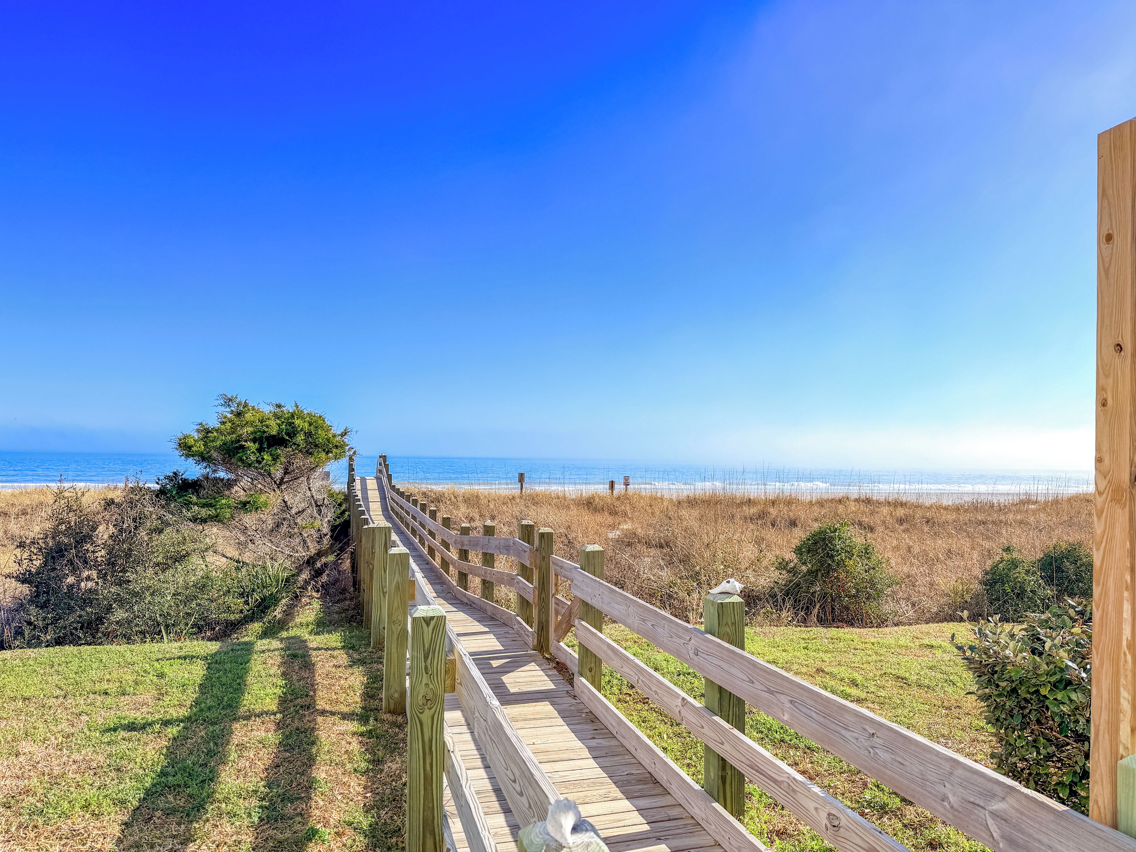 A wooden boardwalk leading to a beach with a clear view of the ocean.