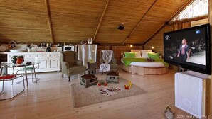 Een gezellige woonkamer met houten plafond, een televisie, een bank en een eettafel met stoelen.