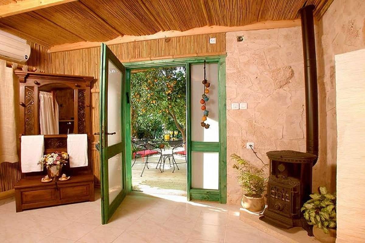 Une porte en bois ouverte donne sur un espace extérieur aménagé avec une table et des chaises, un mur en pierre et un four traditionnel.