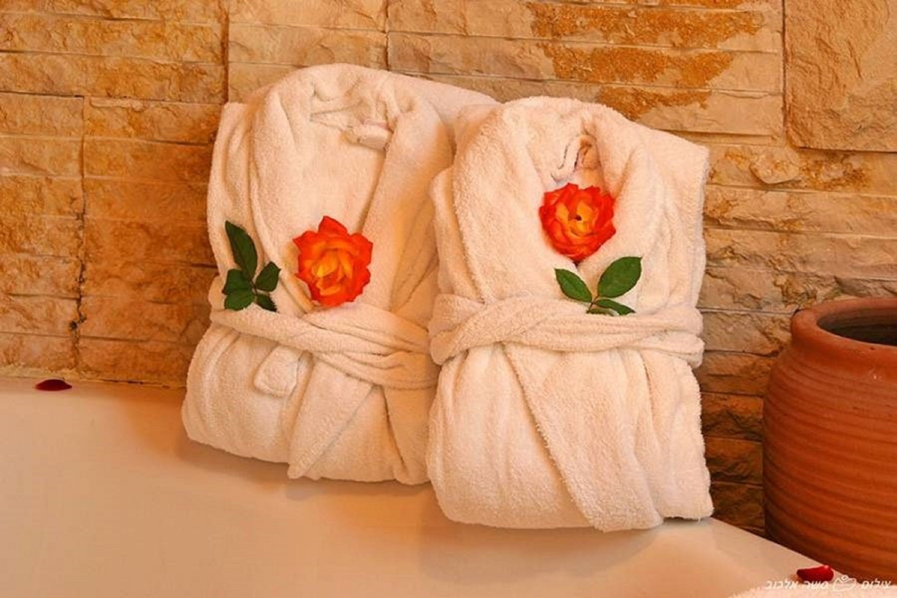 Dos albornoces blancos con rosas rojas atadas, sobre una superficie frente a una pared de piedra.