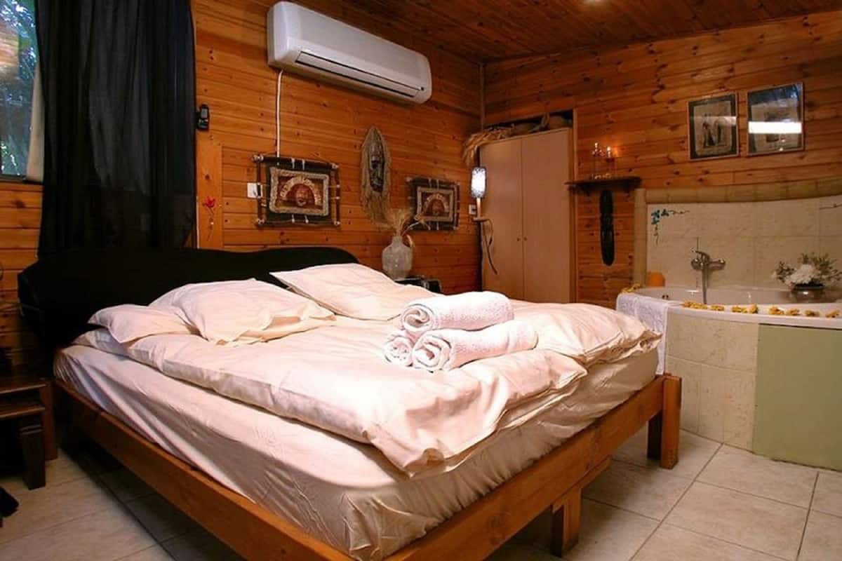 Une chambre à coucher dans une cabane en bois, comprenant un lit, une table de chevet, une coiffeuse avec un miroir et une fenêtre avec des rideaux.