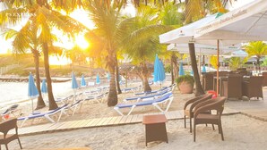 Zona de bar junto a la playa con sillones, sombrillas y mesas al aire libre.
