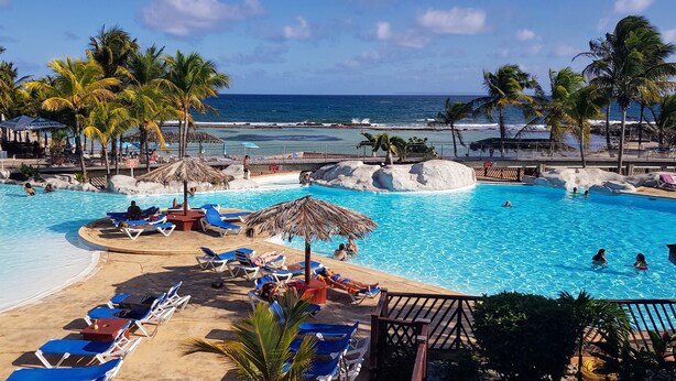 Zona de piscina en un resort, con agua azul cristalina, sillas de descanso y palmeras.