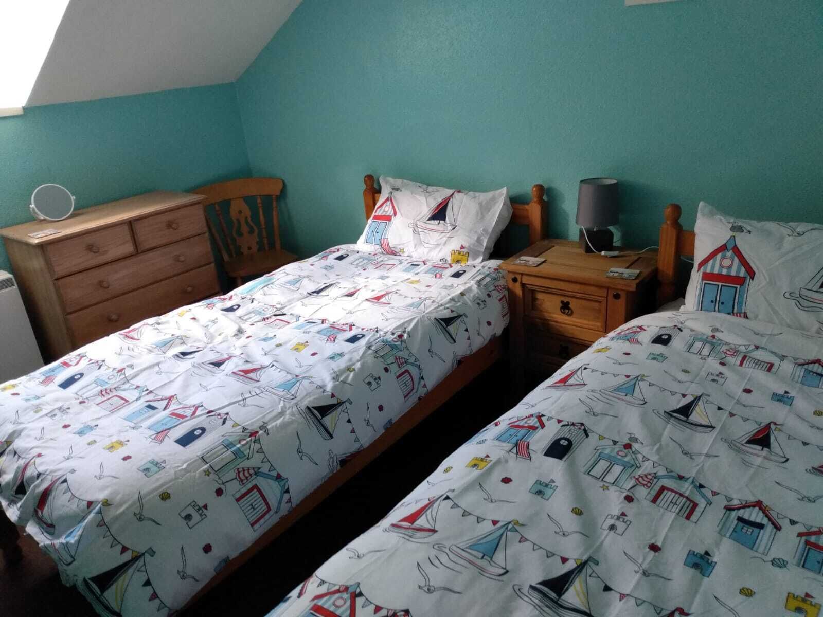 Makuuhuoneessa on kaksi erillistä sänkyä, puinen lipasto, yöpöytä ja lamppu.