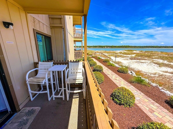 A balcony with white chairs and a table, overlooking a beach with a wooden fence and landscaped garden. - Inlet Point Villas 2A (North Myrtle Beach)